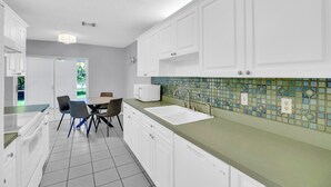 Eine moderne Küche mit weißen Schränken, einer grünen Arbeitsplatte und einer gefliesten Rückwand.