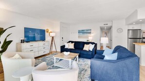 A modern living room with a blue sofa, white armchairs, a coffee table, and a TV on a white cabinet. - Ocean Place 402 | Oceanfront Balcony Views (Ocean City)