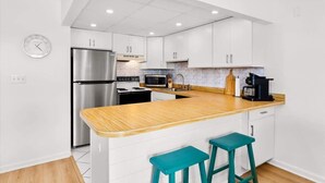 A modern kitchen with white cabinets, stainless steel appliances, a wooden countertop, and teal bar stools. - Ocean Place 402 | Oceanfront Balcony Views (Ocean City)