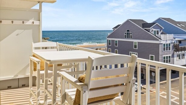 A balcony with a view of the ocean and beach, white furniture, and a building in the background. - Ocean Place 402 | Oceanfront Balcony Views (Ocean City)