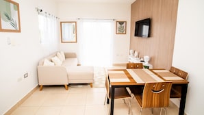 Uma sala de estar moderna com um sofá, uma mesa de jantar com cadeiras, uma televisão de tela plana na parede e uma grande janela com cortinas.