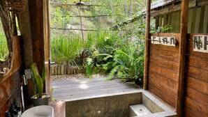 Un baño de madera con una bañera de concreto, un lavamanos y una lámpara colgante.