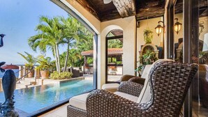 A wicker lounge chair by a pool with a view of palm trees and a patio area. - Mediterranean Waterfront Estate on Caloosahatchee (Fort Myers)