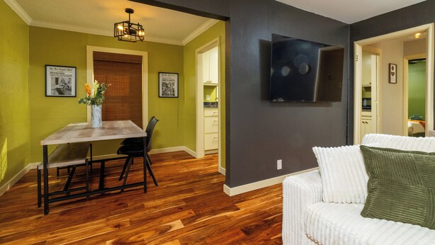 A dining area with a wooden table and chairs, a white sofa, and a flat-screen TV mounted on the wall. - Fenced Yard, Parking + Workspace - Downtown Dallas (Dallas)
