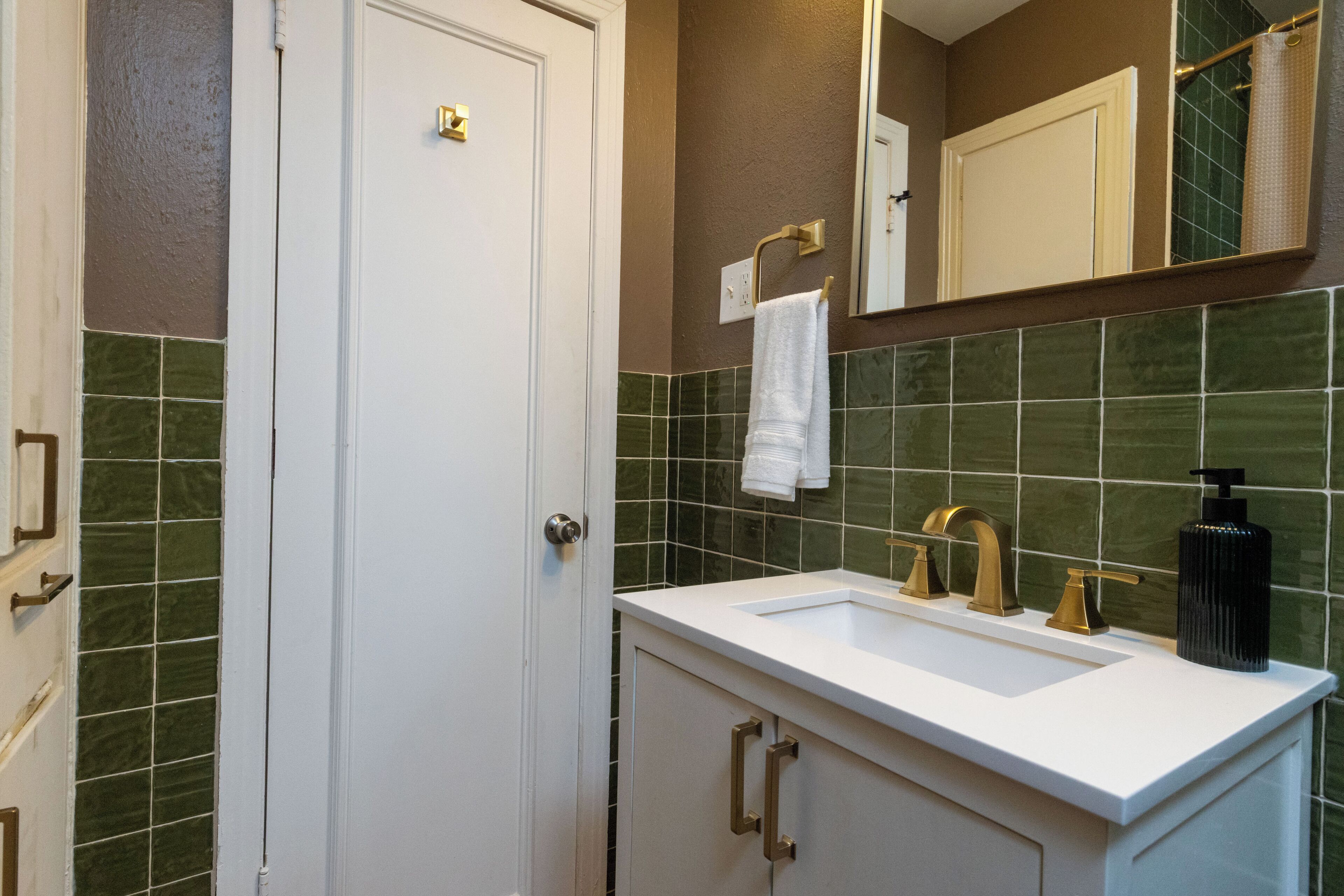 A bathroom with a white sink, gold faucets, and green tiled walls.