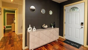 A hallway with a wooden floor, a white door with a glass panel, and a console table with decorative items. - Fenced Yard, Parking + Workspace - Downtown Dallas (Dallas)