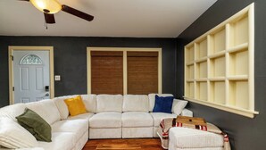 A modern living room with a sectional sofa, a wooden floor, a ceiling fan, and a large window with blinds. - Fenced Yard, Parking + Workspace - Downtown Dallas (Dallas)