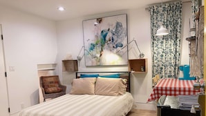 Un dormitorio con cama, una silla, escritorio y refrigerador.