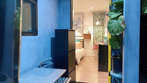 Un pasillo estrecho con una mesa y sillas, que conduce a un dormitorio con una cama, un escritorio y una silla.