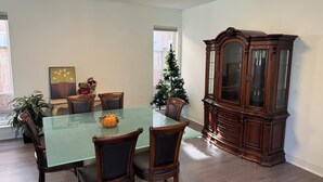 A dining area with a glass-top table, wooden chairs, a dark wooden cabinet, and a Christmas tree.