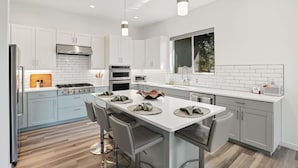 A modern kitchen with white cabinets, a central island with bar stools, stainless steel appliances, and pendant lighting. - Luxury Lodge | Hot Tub + Views | 5 Min to DT (Prescott)
