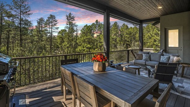 A covered outdoor deck with a wooden table and chairs, a sofa, and a flower vase. - Luxury Lodge | Hot Tub + Views | 5 Min to DT (Prescott)