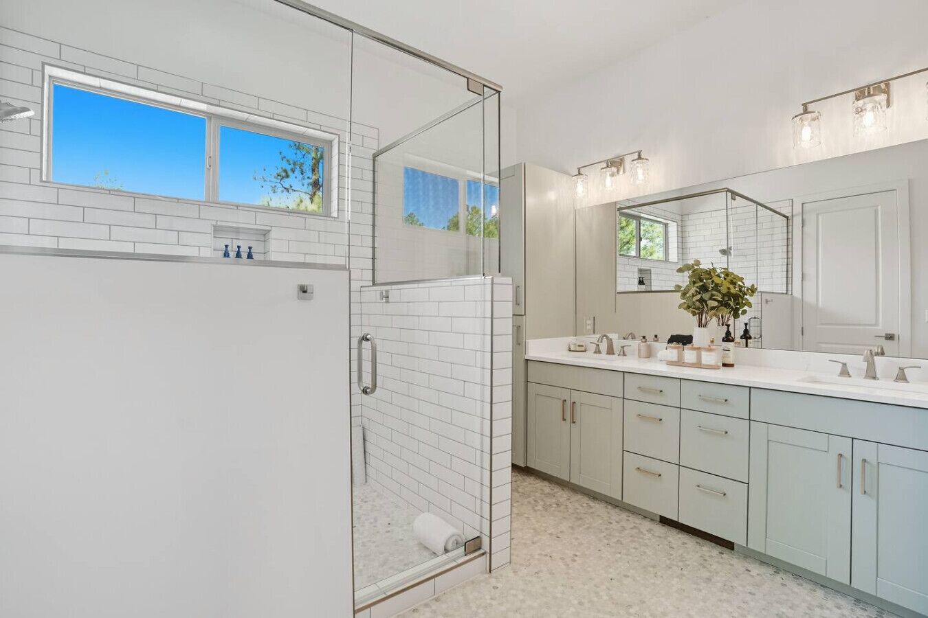Een moderne badkamer met een douchecabine van glas, een grote spiegel en een vloer belegd met witte tegels.