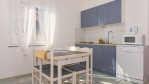 A small kitchenette with a microwave, a sink, and cabinets. There is a table with a chair and a window with curtains. - Amazing apartment in Pirovac with house sea view (Pirovac)