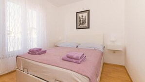 A neatly made bed with pink linens and folded towels, a bedside table with a lamp, and a framed picture on the wall. - Amazing apartment in Pirovac with house sea view (Pirovac)
