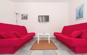 Une pièce avec deux canapés rouges, une petite table blanche, un lampadaire et deux tableaux encadrés accrochés aux murs.