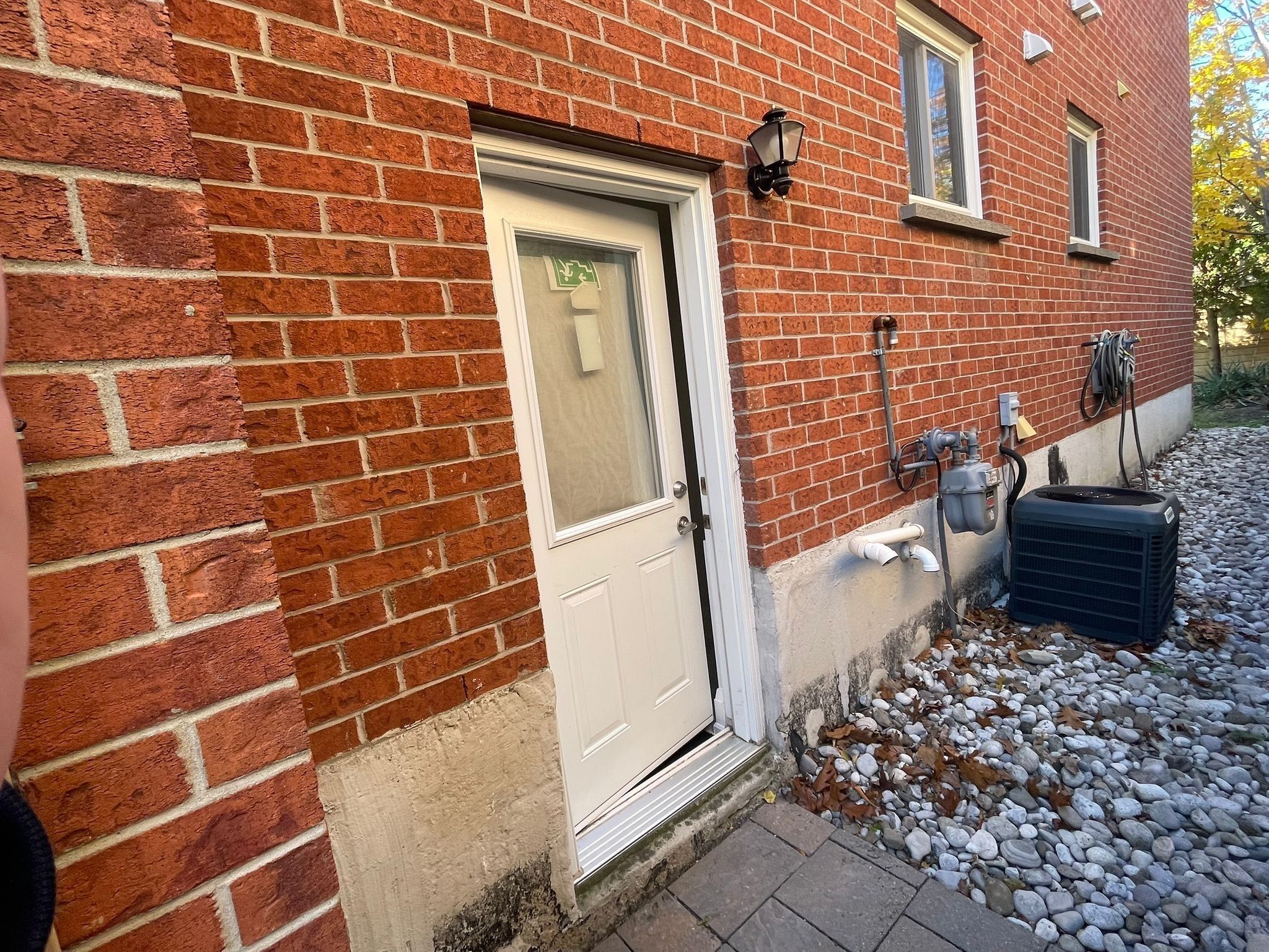 A brick building with a white door, outdoor electrical outlets, and a large air conditioning unit on the ground.