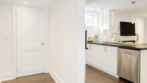 A modern kitchen with white cabinets, a stainless steel dishwasher, and a flat-screen TV mounted above the sink. - Comfortable Mississauga Stay, Private Entry, Laundry & Wi-Fi (Mississauga)