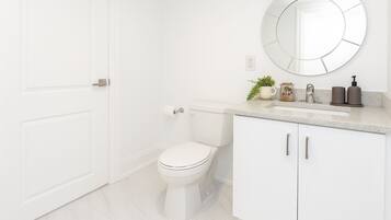 A modern bathroom with a white toilet, a round mirror, and a countertop with toiletries.