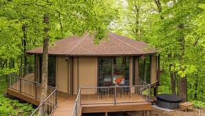 Une terrasse en bois avec une structure vitrée, un jacuzzi et une table avec des chaises.