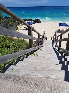 A wooden staircase leading to a beach with blue umbrellas and chairs. - Private pool and private beach in this wonderful Warwick beachfront apartment (Warwick Parish)