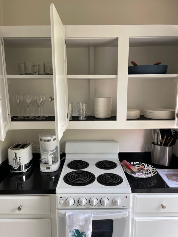 A kitchen with white cabinets, a stove, a coffee maker, and various kitchenware. - Private pool and private beach in this wonderful Warwick beachfront apartment (Warwick Parish)