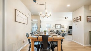 A dining area with a wooden table and chairs, a chandelier, and a view into the living room.