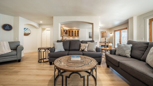 A spacious living room with a large gray sofa, a round coffee table, and a fireplace.