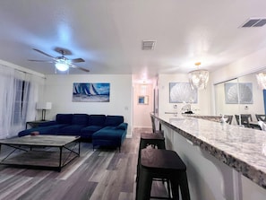 A modern living room with a sofa, a coffee table, and a dining area with a marble countertop and bar stools. - “Quiet Ground‑Floor 2BR/2BA • Pool • No Resort Fees” (Panama City Beach)
