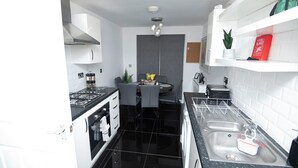 A compact kitchen with black countertops, white cabinets, a gas stove, and a dining area with a table and chairs.