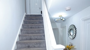A staircase with carpeted steps, white railings, and a wall-mounted light fixture.