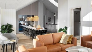 A modern living room with a sofa, a coffee table, and a dining area with a table and chairs. - Cozy home in Glesborg with sauna (Glesborg)
