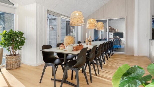 A dining area with a long table, black chairs, wicker baskets, and a potted plant. - Cozy home in Glesborg with sauna (Glesborg)