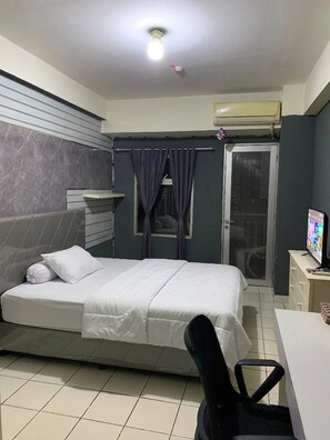 Habitación de hotel con cama, escritorio, aire acondicionado, televisor y puerta corredera que da a un balcón.