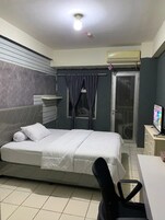 Een hotelkamer met een bed, een bureau, een airconditioner, een televisie en een schuifdeur naar een balkon.