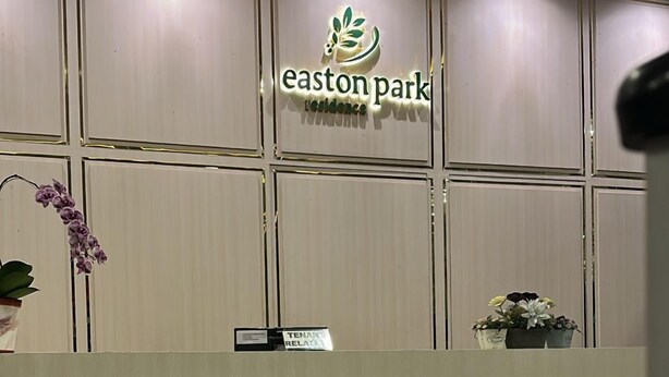 Vastaanottotiski, jossa on Easton Park Residencen logo, kyltti, jossa lukee ”TENANT RELAX” (asukkaille tarkoitettu oleskelutila), ja ruukussa oleva kasvi.