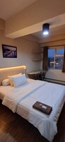 A hotel room with a bed, a desk, a chair, a window with curtains, and a picture on the wall.