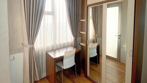 A room with a wooden desk, a chair, a wardrobe with mirrored doors, and a window with curtains. - Apartemen Easton park - Giandara (Cileunyi)