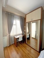 Una habitación con un escritorio de madera, una silla, un armario con puertas espejadas y una ventana con cortinas.