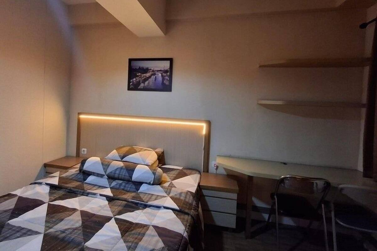 Un dormitorio con cama, escritorio y silla. Hay un cuadro en la pared encima de la cama.