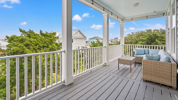 A covered porch with a white railing, wicker furniture, and a view of surrounding houses and trees. - Spacious NEW Luxury 5 Bedroom / 6 Bath Custom Home with Pool and Elevator (North Myrtle Beach)