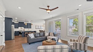 A spacious living area with a grey sofa, striped armchairs, and a coffee table. A ceiling fan and pendant lights are visible. - Spacious NEW Luxury 5 Bedroom / 6 Bath Custom Home with Pool and Elevator (North Myrtle Beach)