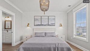 A bedroom with a large bed, a chandelier, a window with blinds, and a view of the outside. - Spacious NEW Luxury 5 Bedroom / 6 Bath Custom Home with Pool and Elevator (North Myrtle Beach)