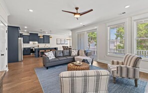 A spacious living area with a grey sofa, striped armchairs, and a coffee table. A ceiling fan and pendant lights are visible. - Spacious NEW Luxury 5 Bedroom / 6 Bath Custom Home with Pool and Elevator (North Myrtle Beach)