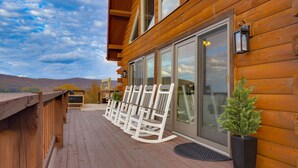 A wooden deck with white rocking chairs and a potted plant, overlooking a mountainous landscape. - Whether you`re looking for a romantic getaway or a fun-filled family vacation, this cabin is the perfect destination for you. (Herndon)