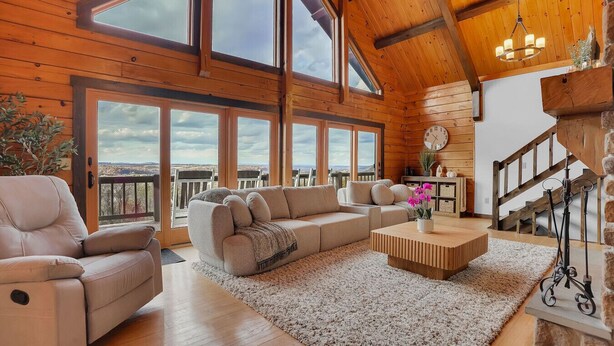 A spacious living room with a large sofa, a coffee table, and a view of the landscape through large windows. - Whether you`re looking for a romantic getaway or a fun-filled family vacation, this cabin is the perfect destination for you. (Herndon)