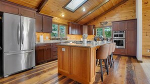 A spacious kitchen with wooden cabinets, a stainless steel refrigerator, a central island with bar stools, and a skylight. - Whether you`re looking for a romantic getaway or a fun-filled family vacation, this cabin is the perfect destination for you. (Herndon)