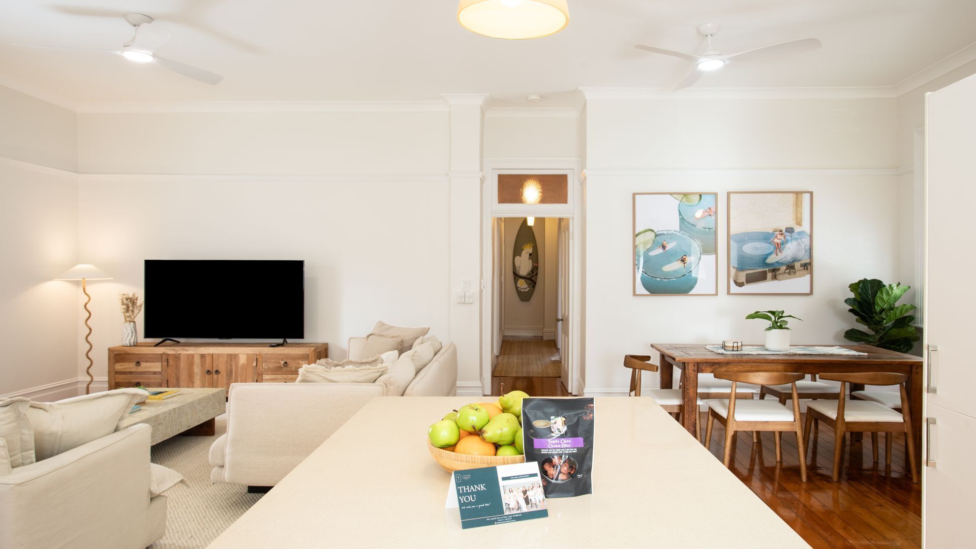 Ein modernes Wohnzimmer mit Flachbildfernseher, ein Essbereich mit Holztisch und Stühlen sowie ein Flur, der zu einem weiteren Zimmer führt.