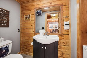 A bathroom with wooden paneling, a white sink, a mirror, and a towel rack with a 'Makeup' towel. - Firefly Holler by Beyond Expectations w Hot Tub (Pigeon Forge)