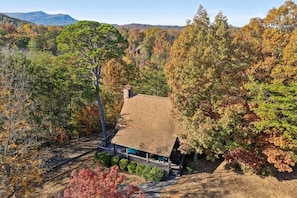 A cabin with a sloped roof, surrounded by dense trees with autumn foliage, set in a mountainous area. - Firefly Holler by Beyond Expectations w Hot Tub (Pigeon Forge)